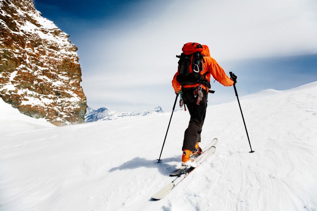 Man climbing on backcountry skis in red coat on a clear day|Portrait of young woman skier in a bright jacket and blue helmet.