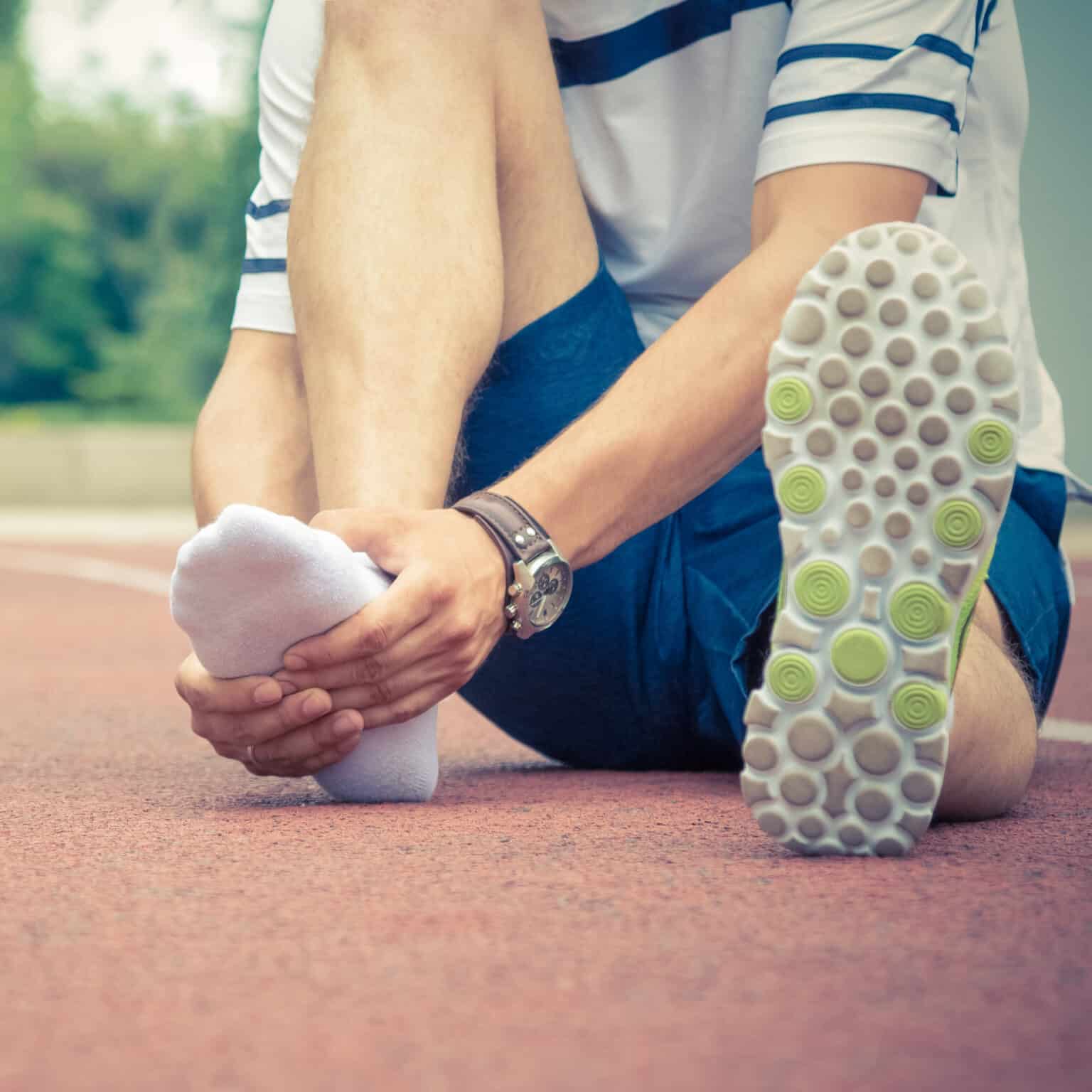 Jogger hands on foot. He is feeling pain as his ankle or foot is broken or twisted. Accident on running track during the morning exercise. Sport accident and foot sprain concepts.